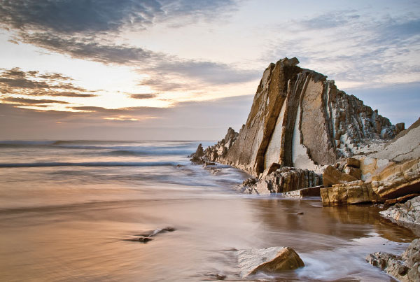 Ocean sunrise next to a tall rock