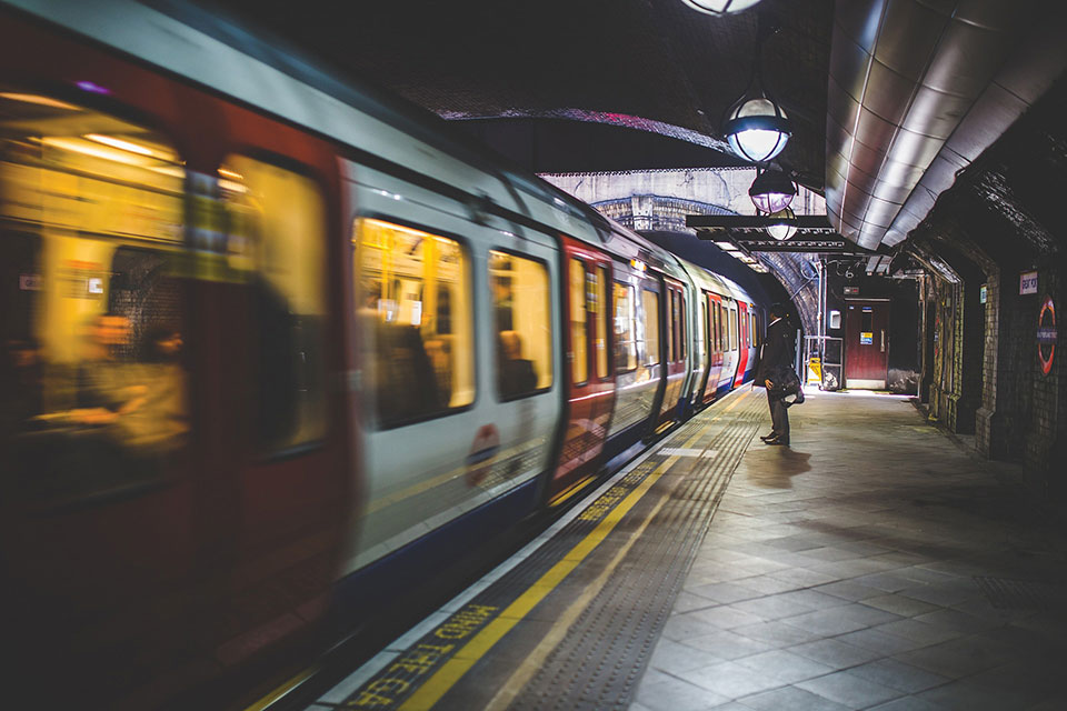 A lone figure stands in the polarized light of the subway at night as a train passes in front of him