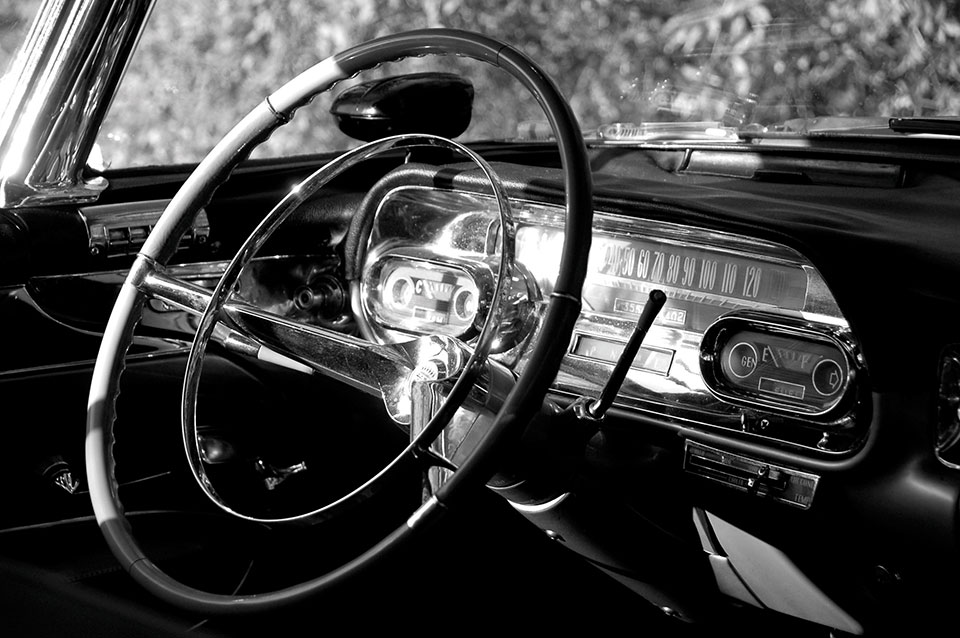 A black and white photograph of the interior of a vintage Cadillac with the focus on the steering column and gauges