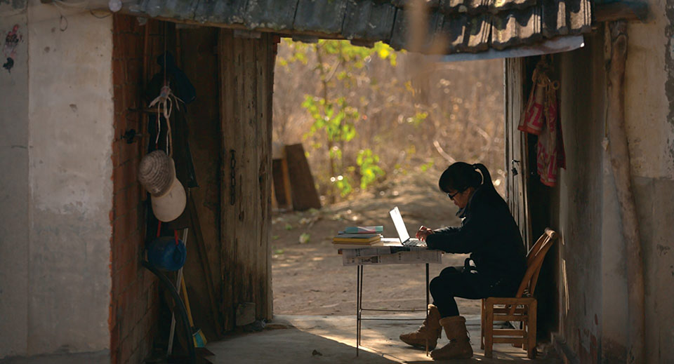 A photograph of the writer Yu Xuiha sitting in an open room typing on a laptop