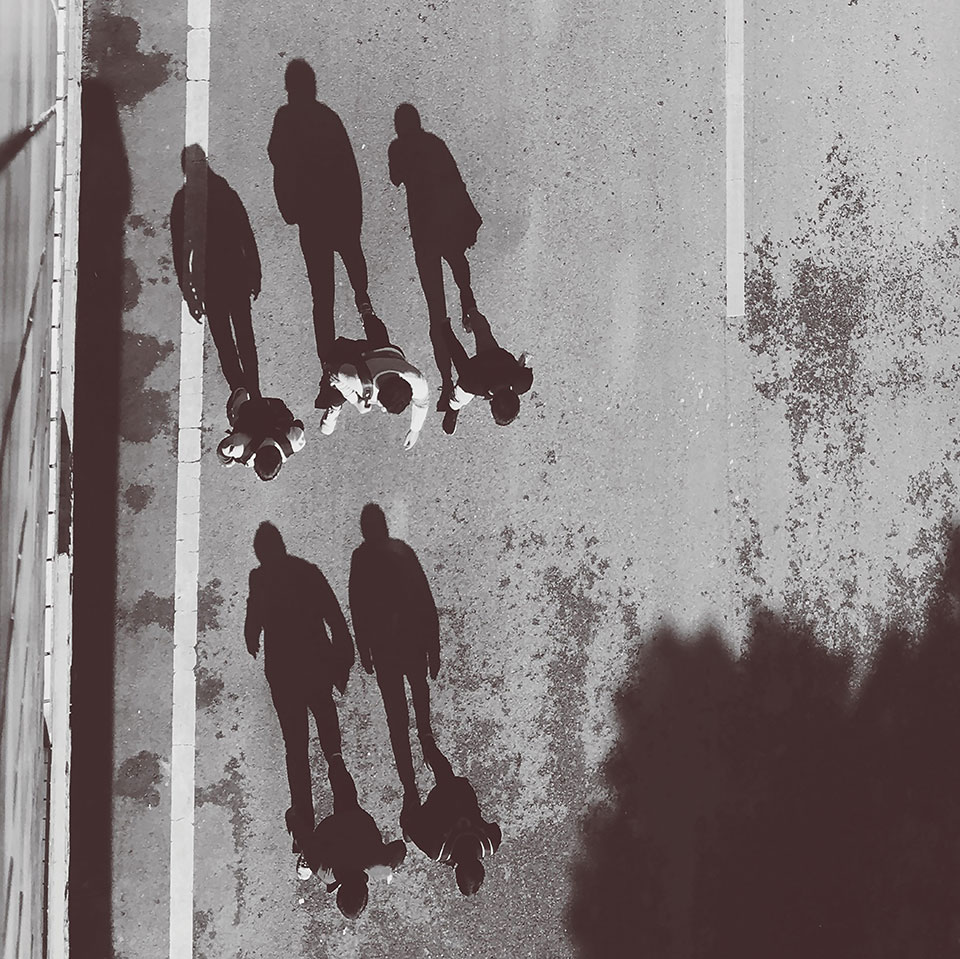 Three youths photographed from above, their shadows producing three upright figures trailing behind them