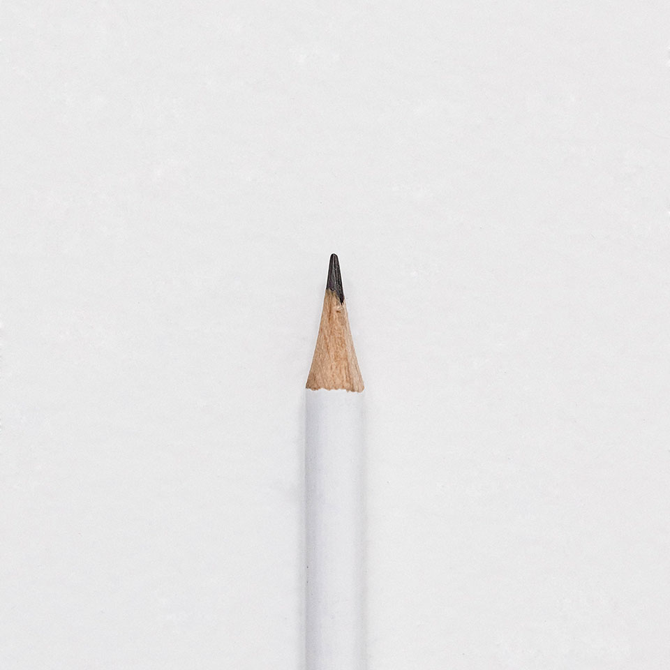 The tip of a white pencil laying on a piece of white paper