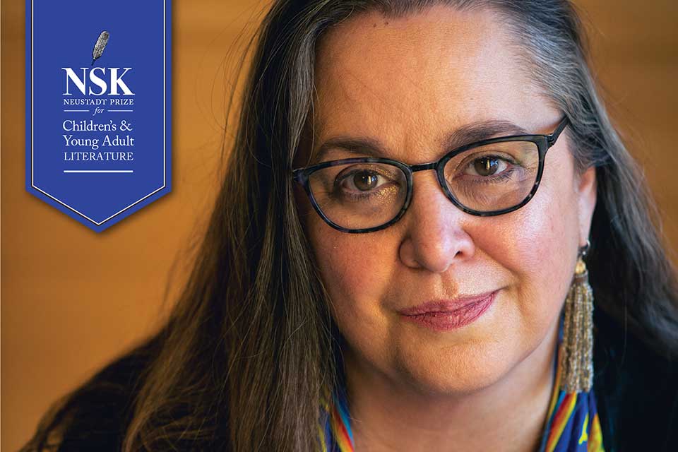 A photograph of Cynthia Leitich Smith with a decorative ribbon identifying her as the 2021 NSK Laureate