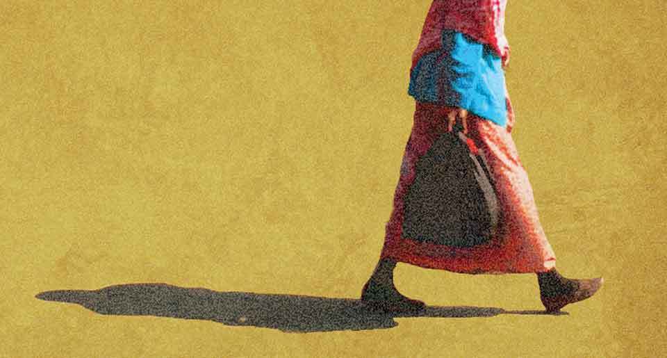 An image of the bottom half of a person walking across the sand with a shadow stretching out behind