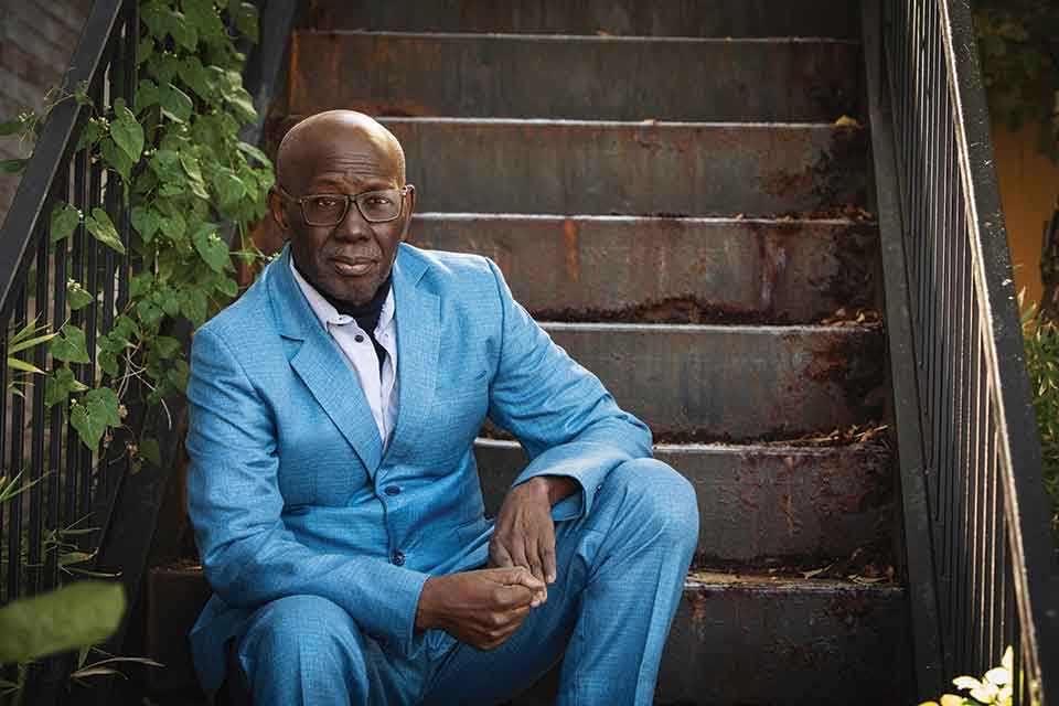 A photograph of Boubacar Boris Diop sitting on stairs looking at the camera