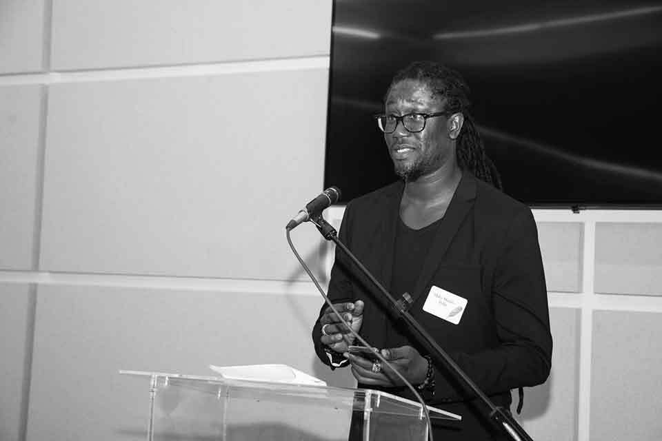 A black and white photograph of Maky Madiba Sylla speaking at a lectern