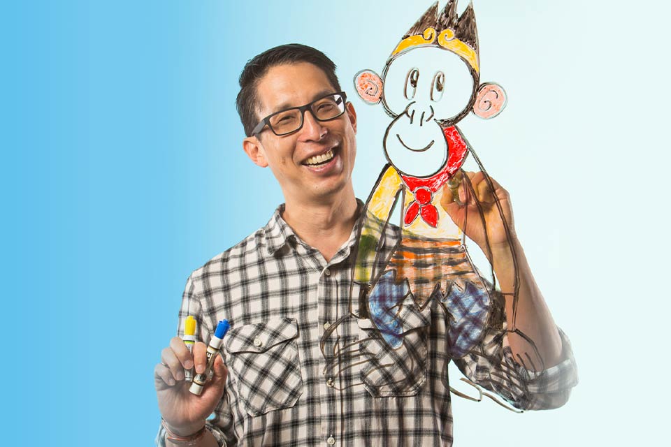 A photograph of Gene Luen Yang drawing a monkey on a plate of glass