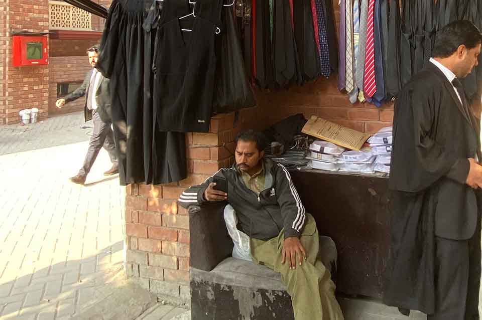 A vendor sits looking at his phone in front of a rack of lawyers' robes