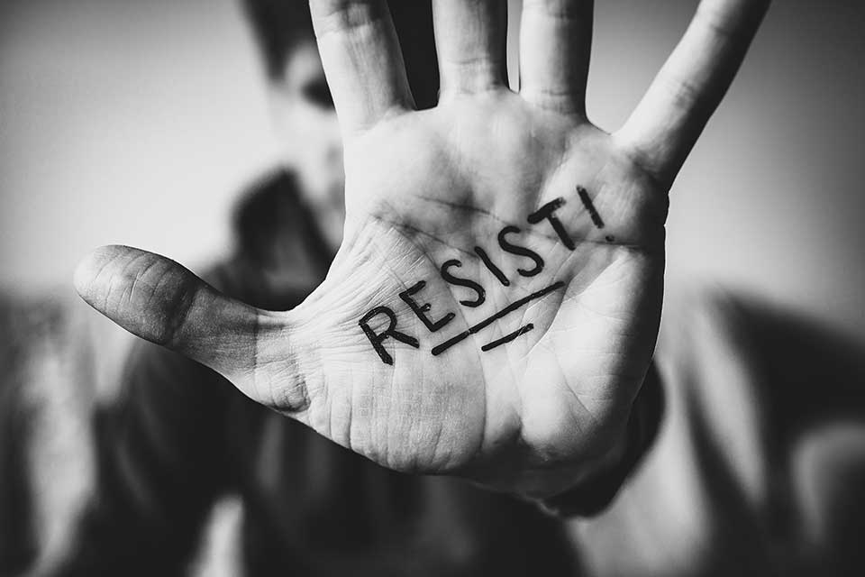 A black and white photograph of a hand with the word Resist written on the palm