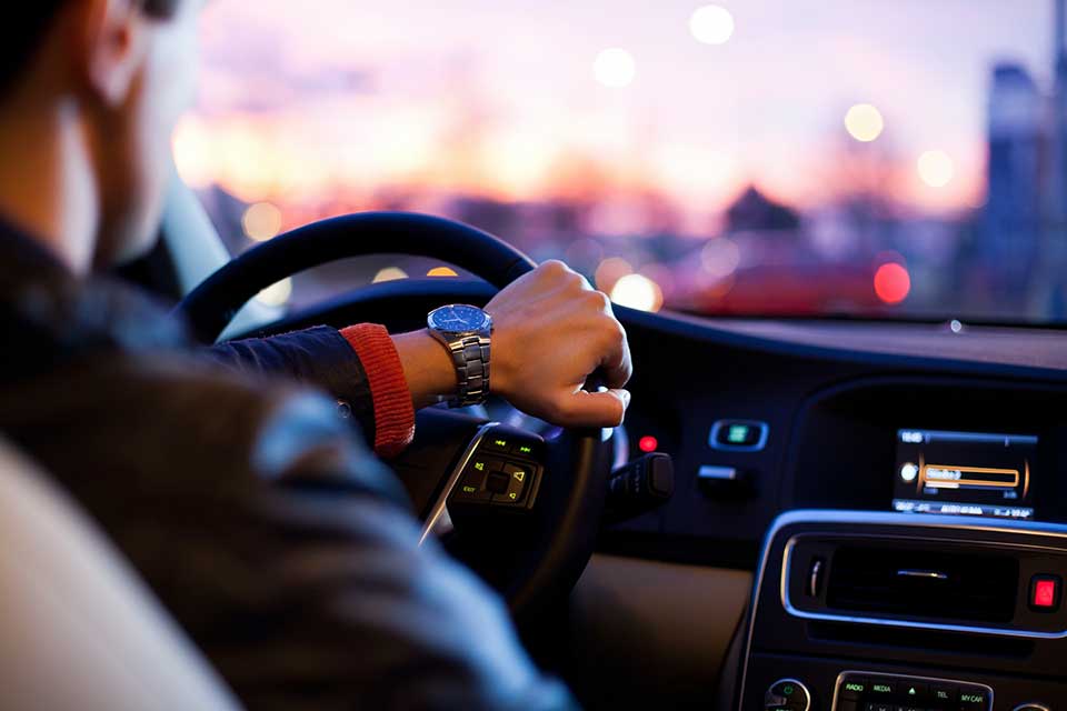 A photograph taken from over the shoulder of a man driving a car