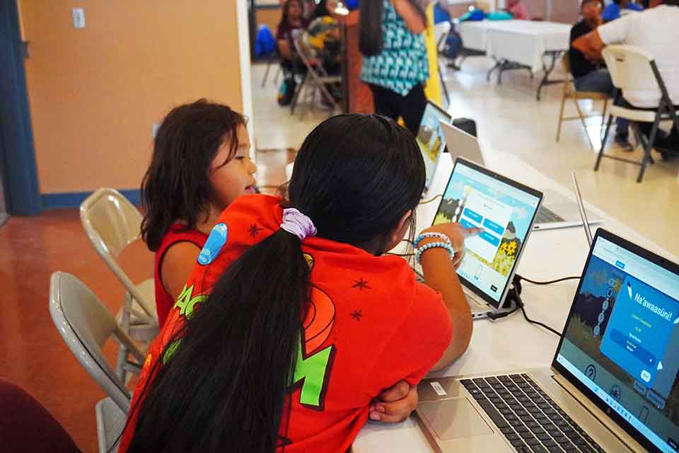 Two children study language materials on a computer