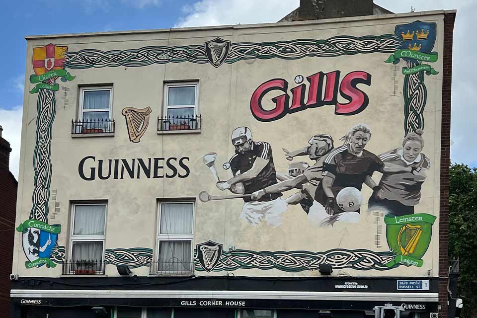 A mural on the side of a building. The mural shows sports figures and the text reads: Guiness. Gills.