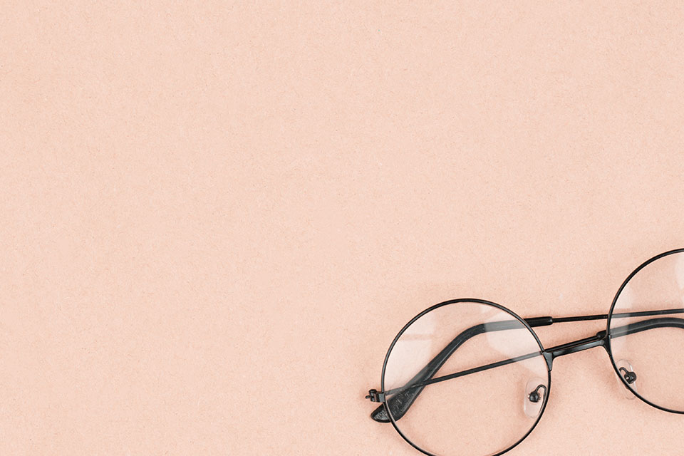 A photograph of round lensed glasses resting against a peach background