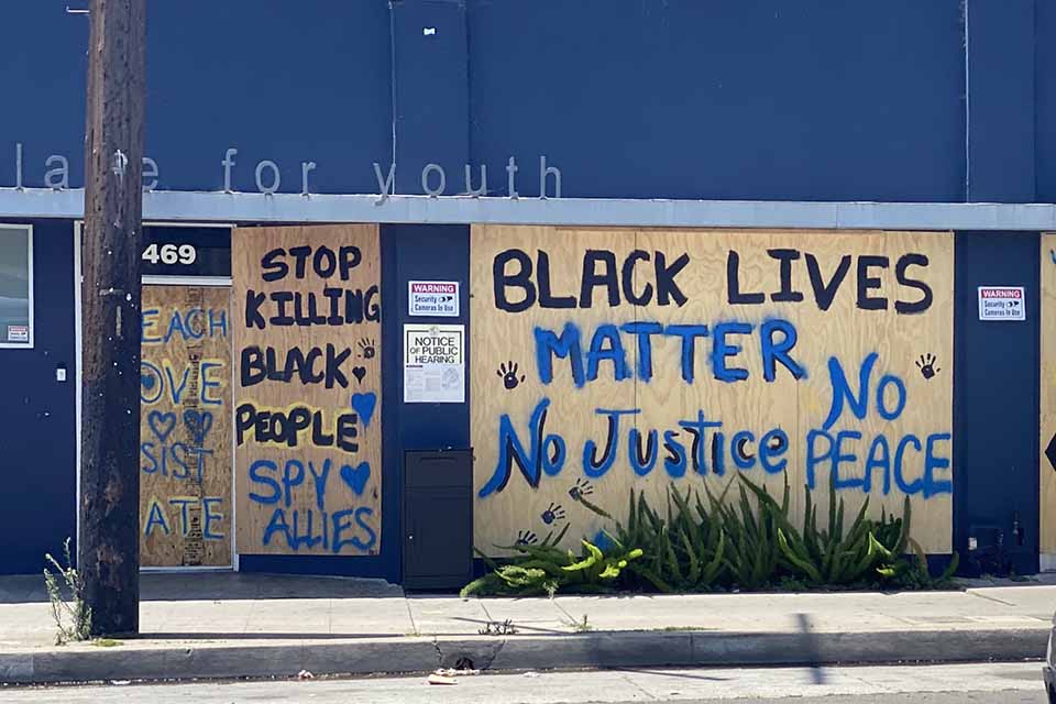 Spray painted words adorn the side of a boarded up building. Text reads: Stop killing black people. Black Lives Matter. No justice. No peace.