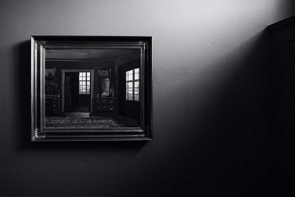 A shadowy black and white photograph of a mirror with windows reflected in it. Photo by Wilhelm Gunkel / Unsplash.