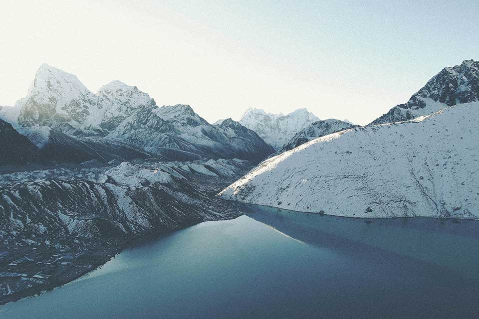 A landscape shot of snow-covered glaciers skirted by an apron of lakes