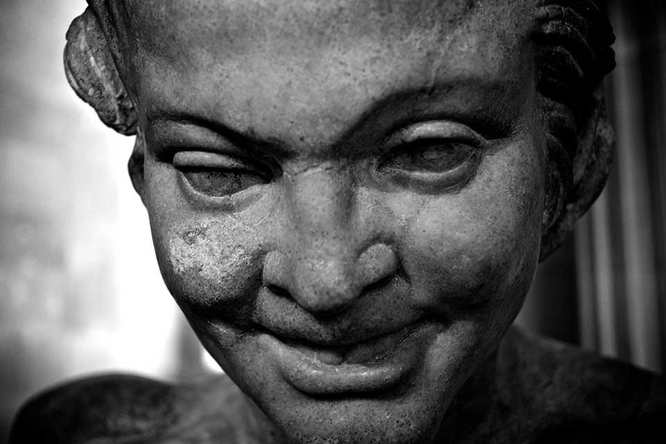 A black and white photograph of a grimacing face rendered in stone