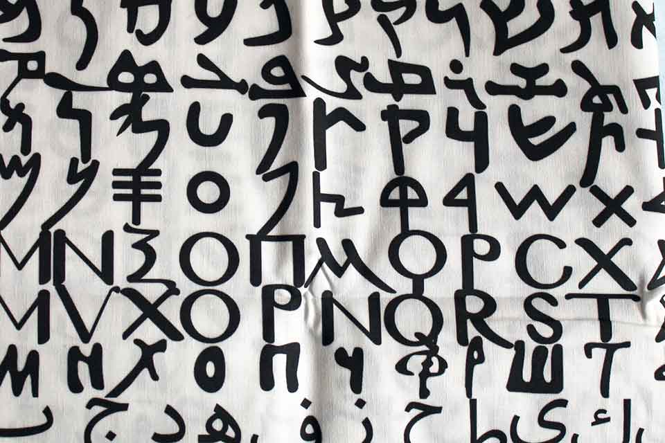 A photograph of the alphabet, each line in a different script, painted on a loose, white cloth