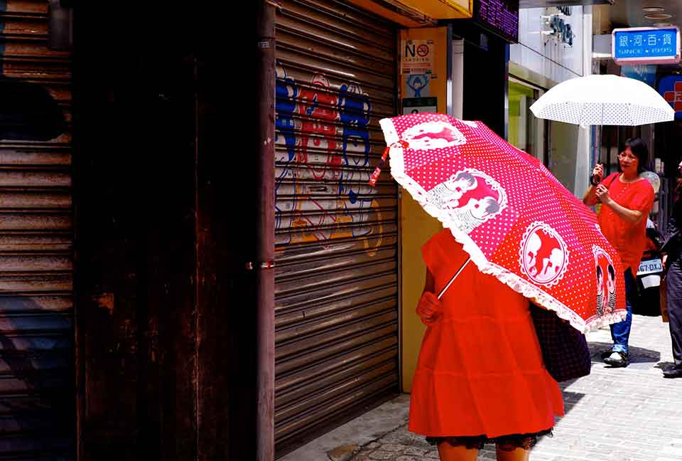 A woman, dressed in red, walks down the street, her face obscured by a red umbrella