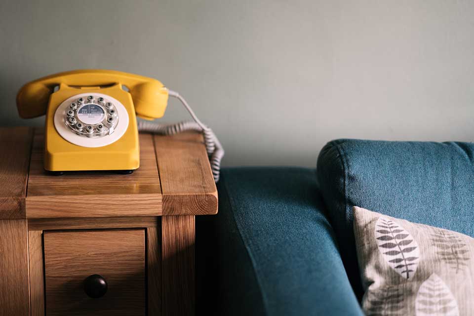 A photograph of a yellow telephone sitting on a wood table next to a blue couch