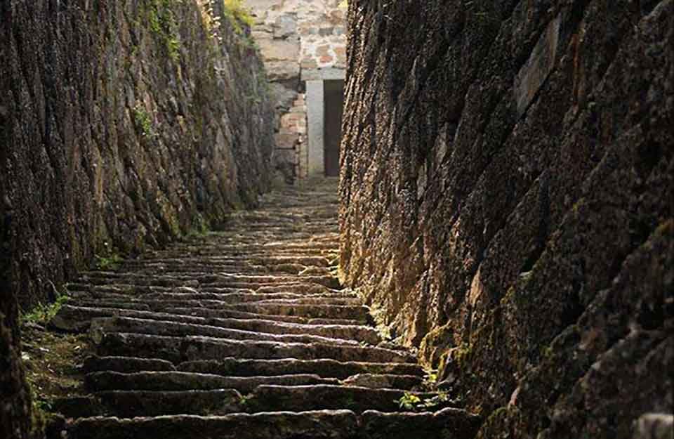 Steps, roughly cut from stone, leading steeply toward a door, partially obscured by the curvature of the rock