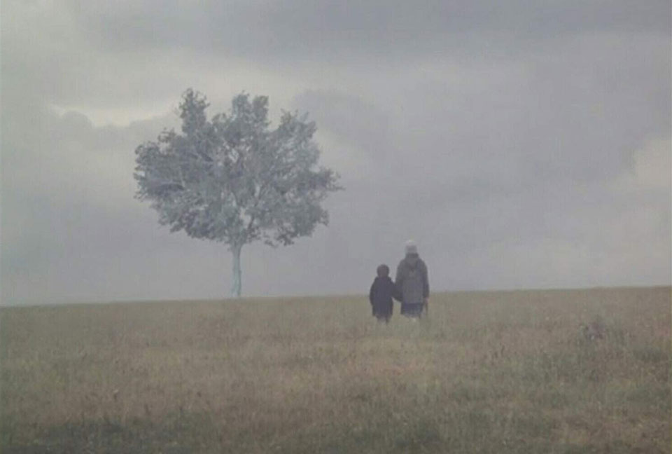 Two figures, presumably parent and child, standing in a gauzy fog, standing in a meadow with a lone tree looming ahead of them