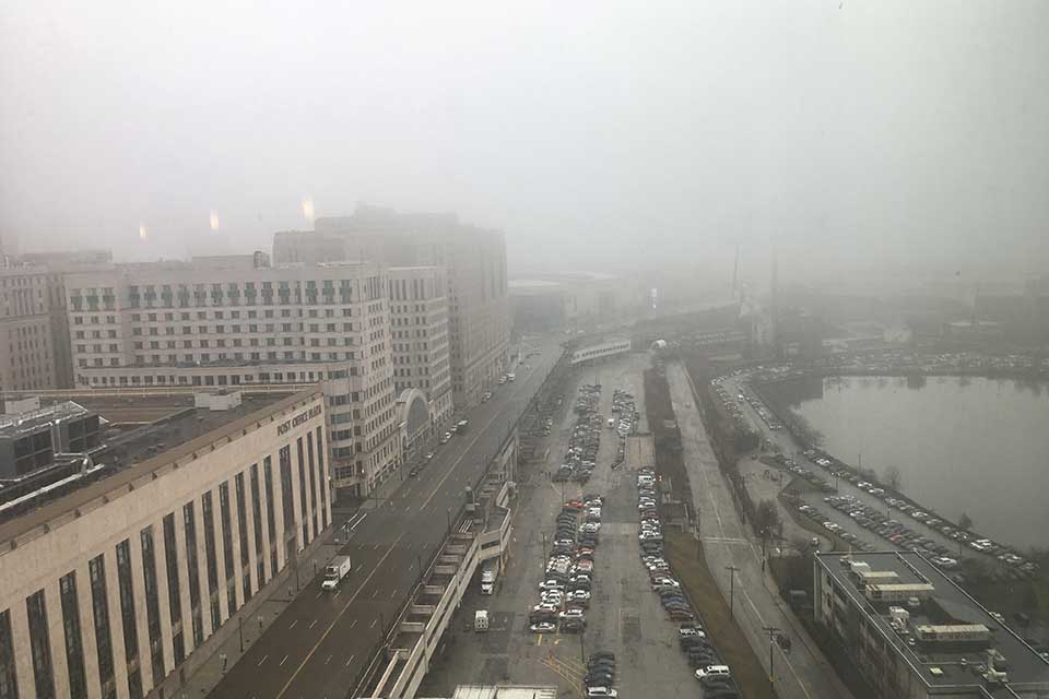 An aerial photograph of a crowded parking lot on a waterfront, shrouded in fog