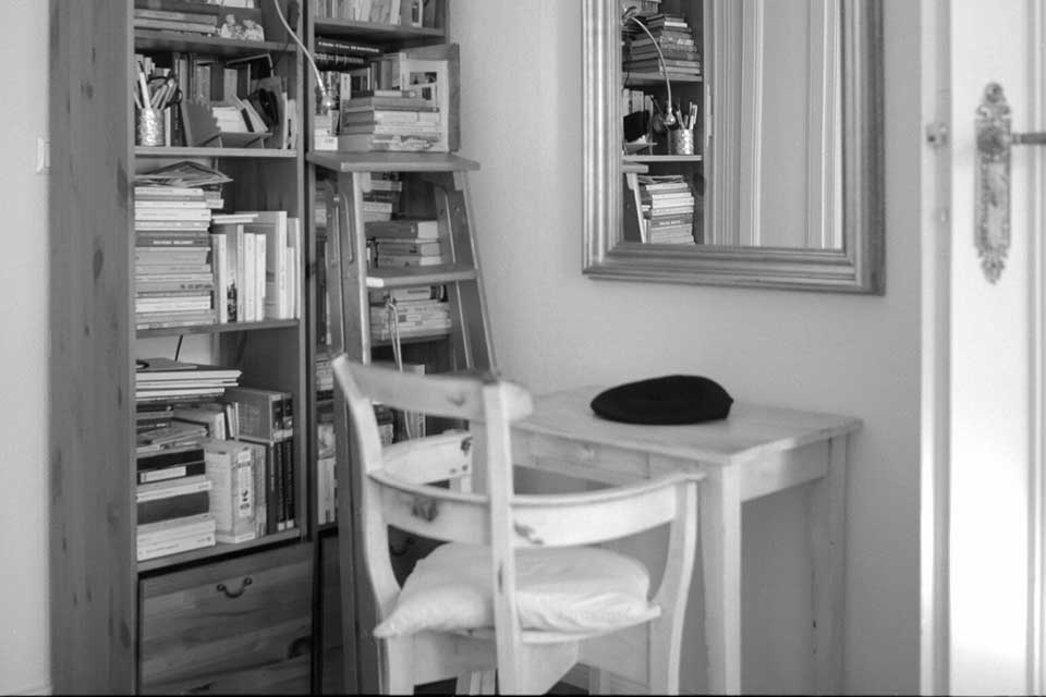 A black and white photo of a chair and desk sitting next to a bookshelf