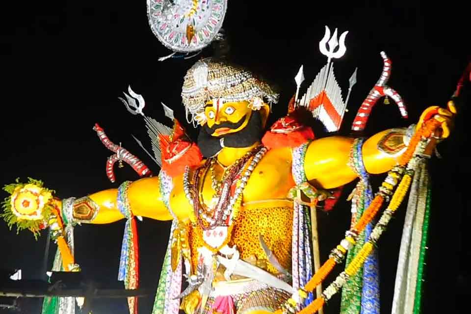 A photo of a Hindu god, wrapped in a turban, strongly lit from below with darkness behind