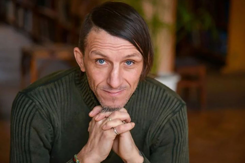 A photograph of author Volodymyr Vakulenko, his hands clasped under his chin as he looks at the camera