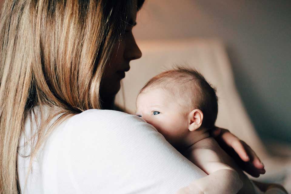 A photograph of a woman holding a baby. Her face is in shadow