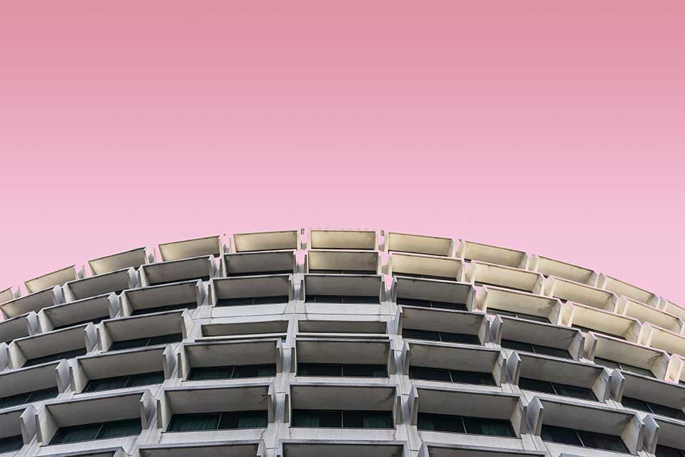 A photograph looking up at a curved building face, with windows fluted open, with a lavender sky above