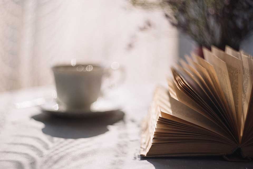 A teacup sits, out of focus, next to a book on a table.