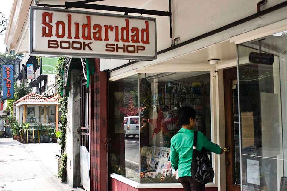 A photograph of a woman in a green jacket entering a book store. A sign above reads, “Solidaridad”