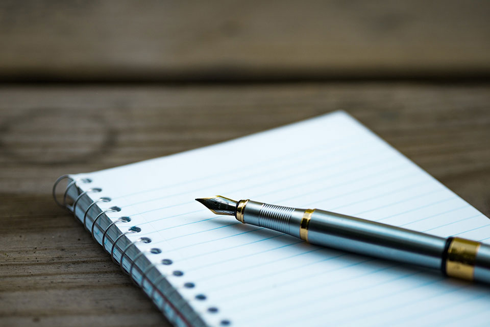 A fountain pen rests on a notebook of lined paper