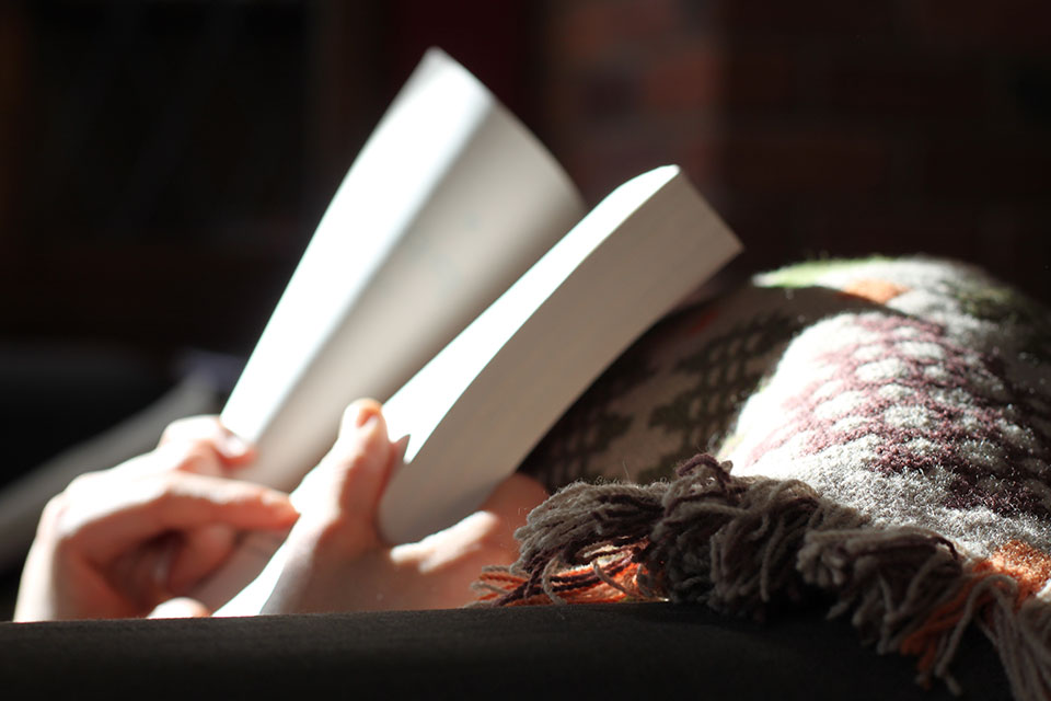 An open book in partial sunlight being held by a person with a blanket.