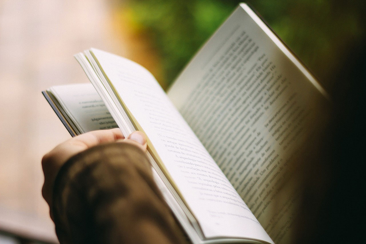 A girl reading a book and wearing a sweater.