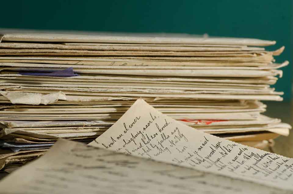 A photo of a stack of papers in front of a solid dark green background. A smaller stack sits in front where the handwritten letters are visible.