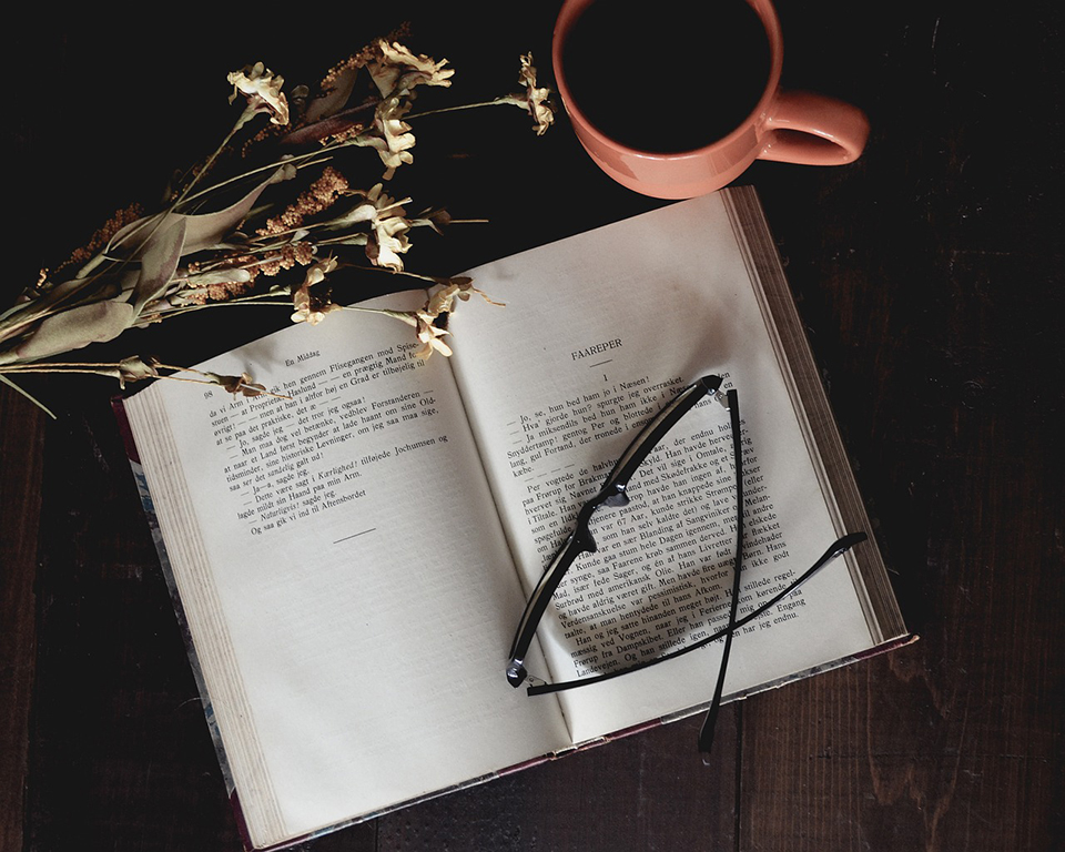 An open book with glasses and a cup of coffee