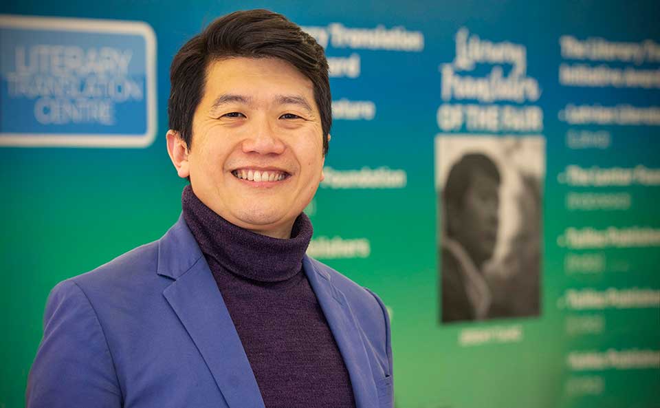 Jeremy Tiang posing in front of materials at the London Book Fair