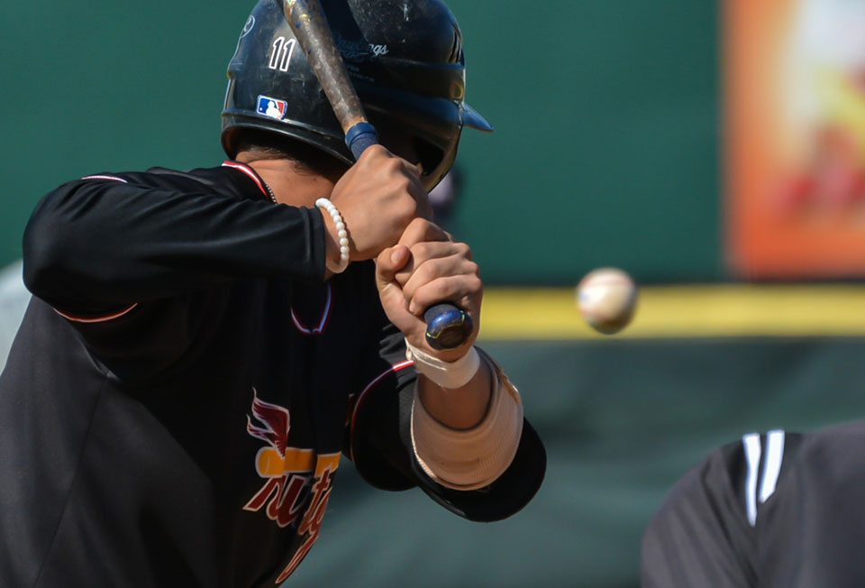 A photograph taken from behind a poised batter as a baseball appears to hang in mid-air in front of him