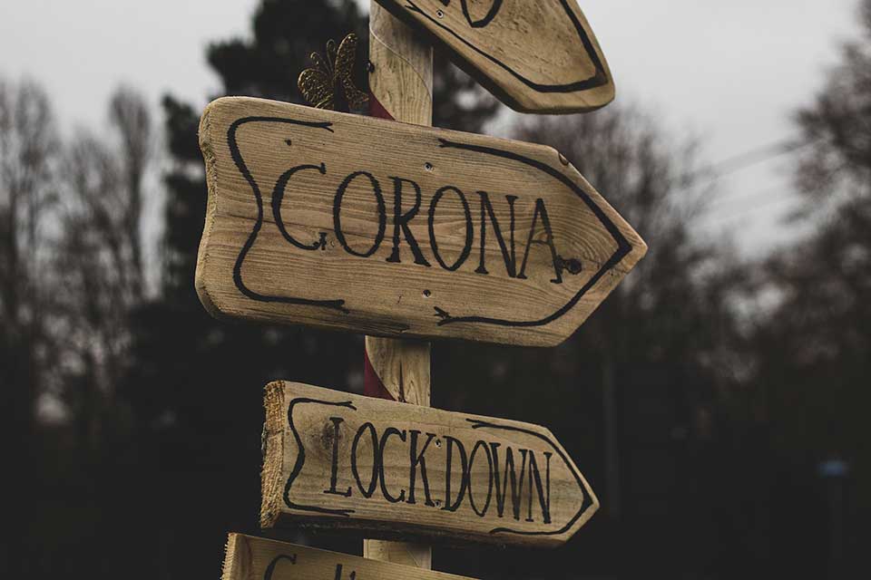 A photograph of a sign. One one arrow, text reads: Corona. On another, text reads: Lockdown.