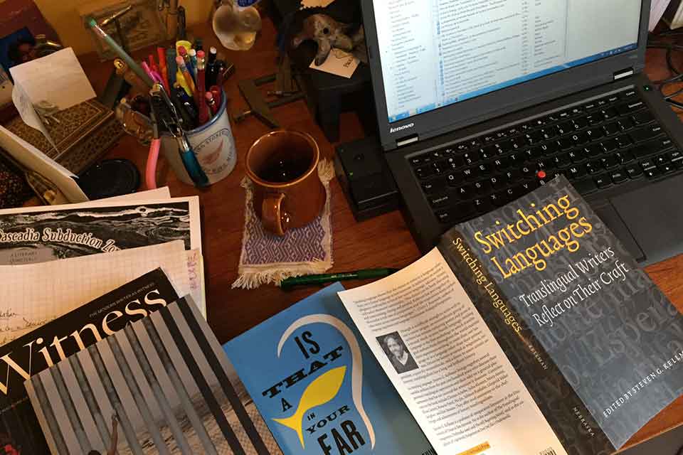 A top down photograph of a desk cluttered with books and a computer monitor nearby