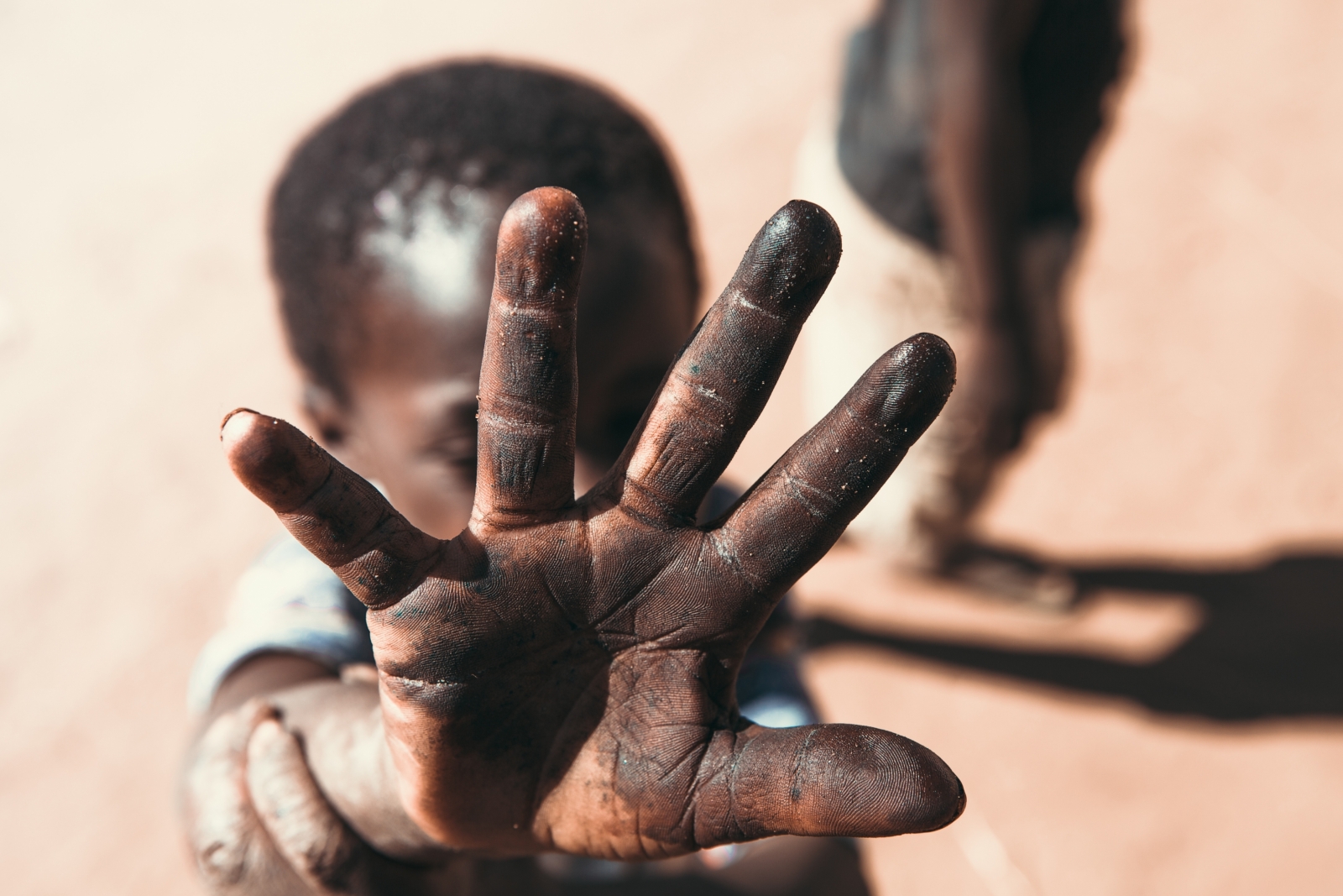 A photo of a young boy holding his hand up towards a camera, partially obscuring his own face