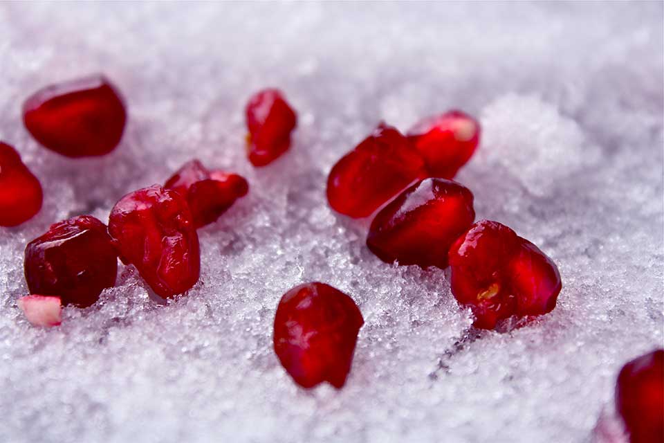 A photograph of dark crimson pomegranate seeds delicately laid out on snow