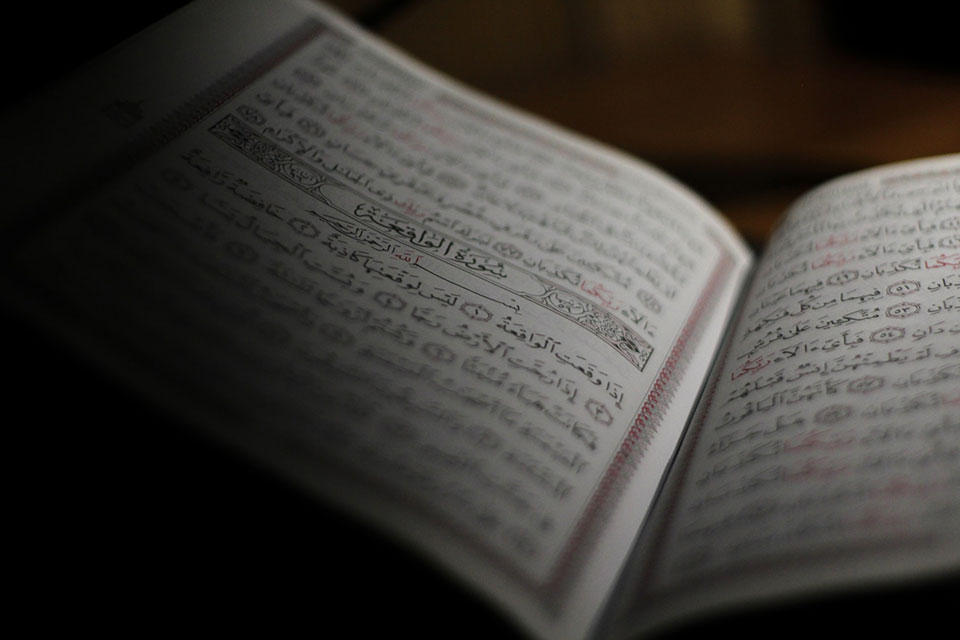 An open book written in Arabic, mostly shrouded in shadow