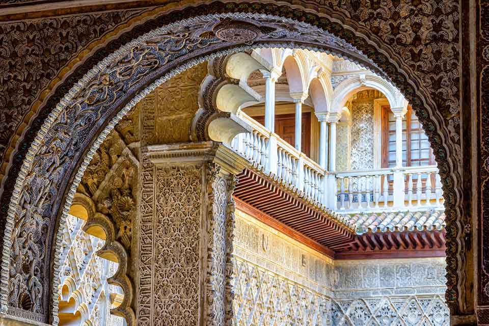 A photograph from inside of an archway that looks toward a balcony in the courtyard outside