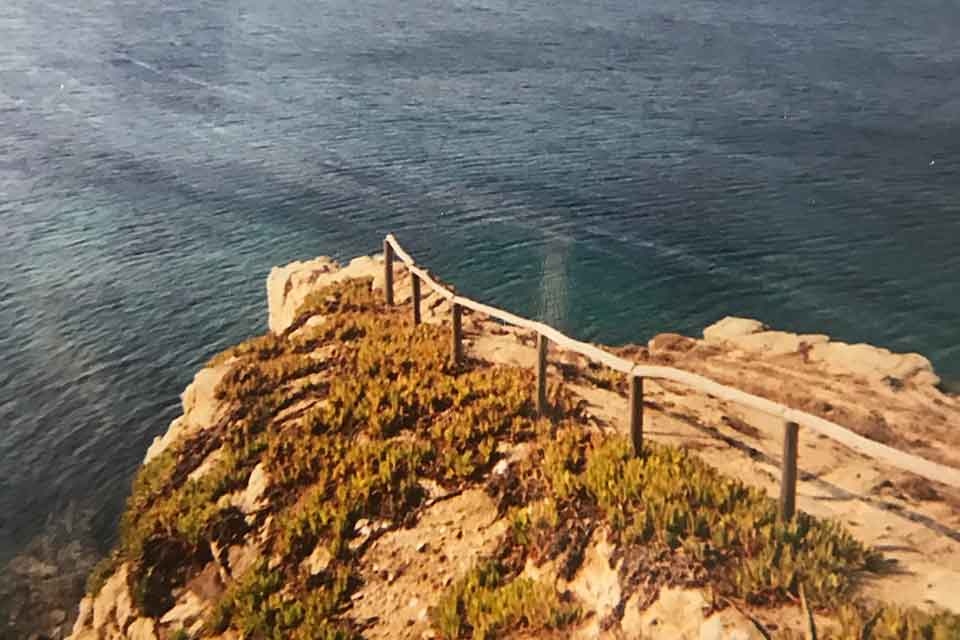 A rough dirt road terminates at the end of a point that sits on a cliff above a wine-dark sea