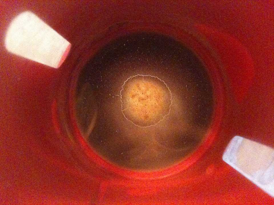 Coffee dregs sitting at the bottom of a red cup, as shot from above