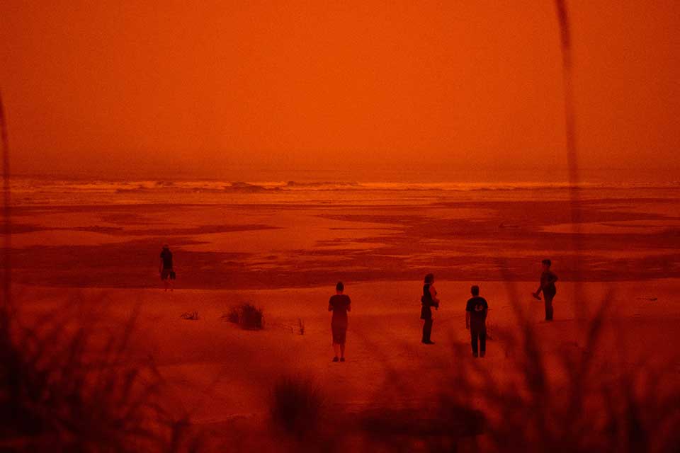 A photograph of figures on a beach. The photograph is heavily colored in red and orange tones.